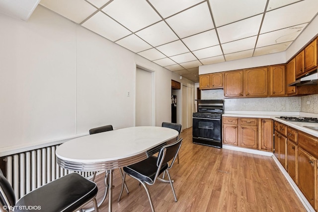 kitchen featuring light countertops, under cabinet range hood, gas stove, light wood-style flooring, and brown cabinets