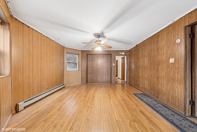 unfurnished room featuring a ceiling fan, wooden walls, baseboard heating, and light wood finished floors