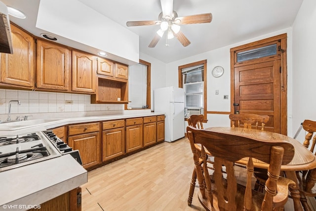 kitchen with light countertops, decorative backsplash, a sink, freestanding refrigerator, and light wood-style flooring