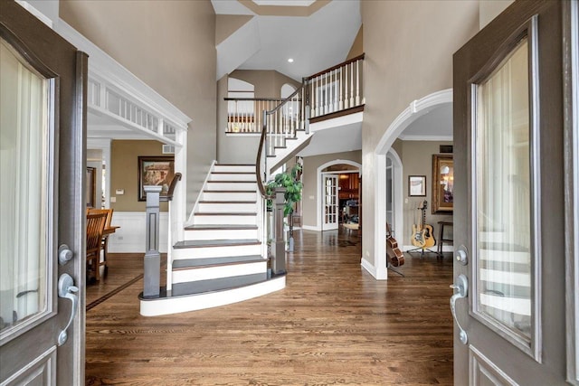 entrance foyer with arched walkways, wood finished floors, a towering ceiling, and stairway
