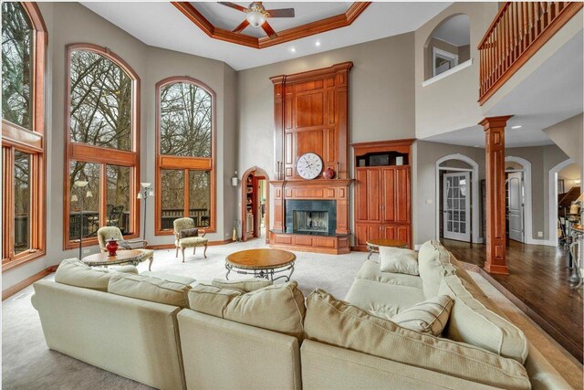 living room featuring a ceiling fan, baseboards, a raised ceiling, a high ceiling, and ornate columns
