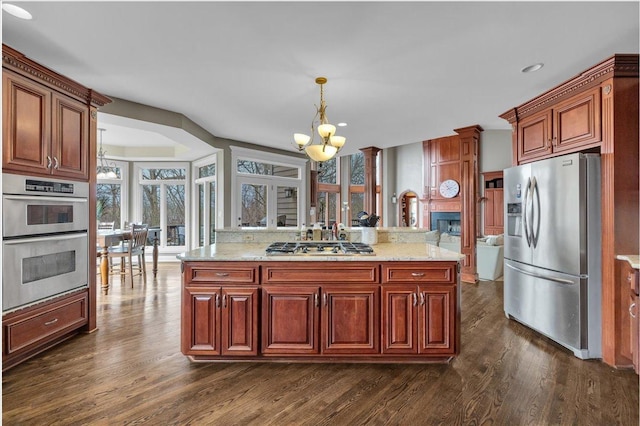 kitchen featuring a chandelier, stainless steel appliances, a fireplace, decorative light fixtures, and dark wood-type flooring