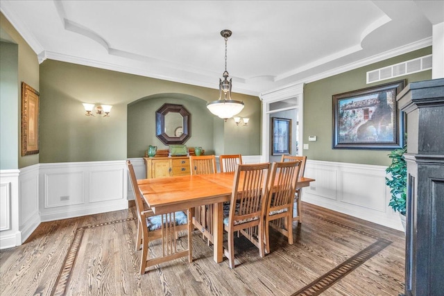 dining space featuring a tray ceiling, wood finished floors, crown molding, and wainscoting