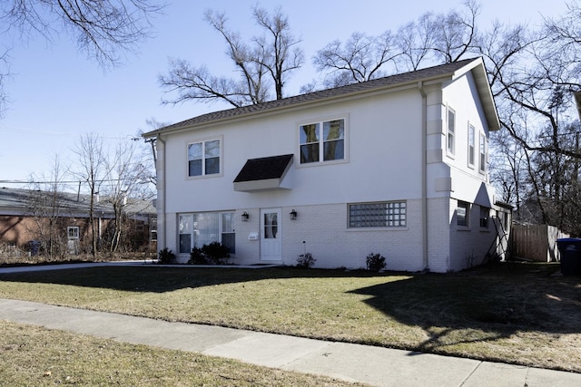 view of front facade featuring stucco siding, a front yard, and brick siding