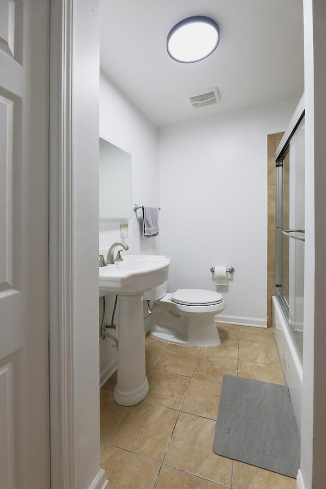 full bath with tile patterned flooring, shower / bath combination with glass door, toilet, a sink, and visible vents