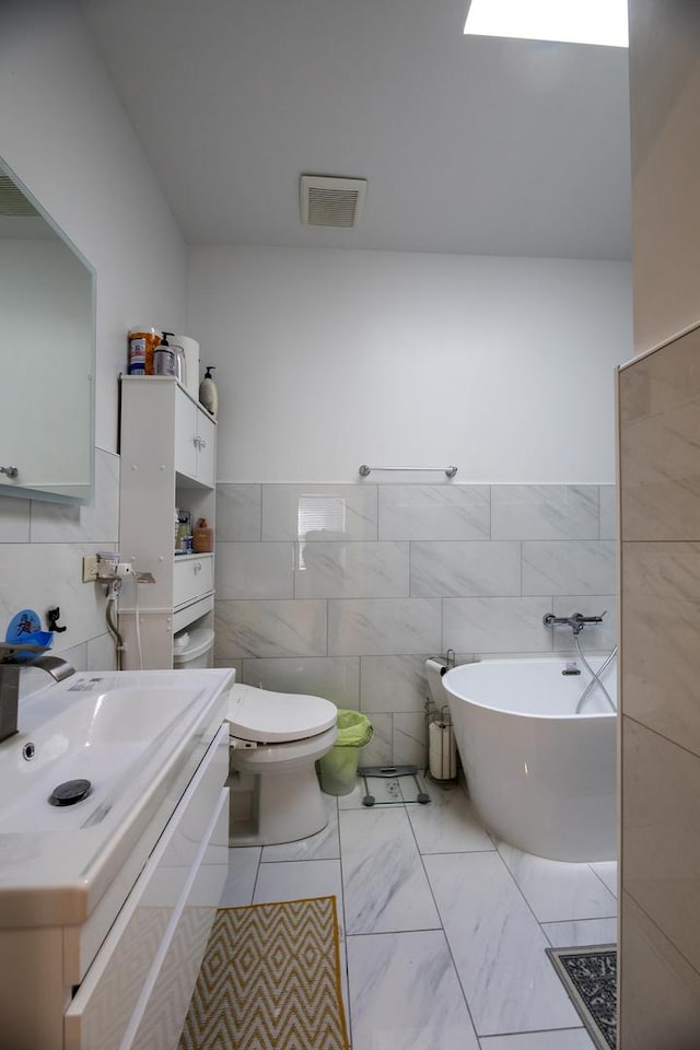 bathroom with a freestanding tub, toilet, vanity, marble finish floor, and tile walls