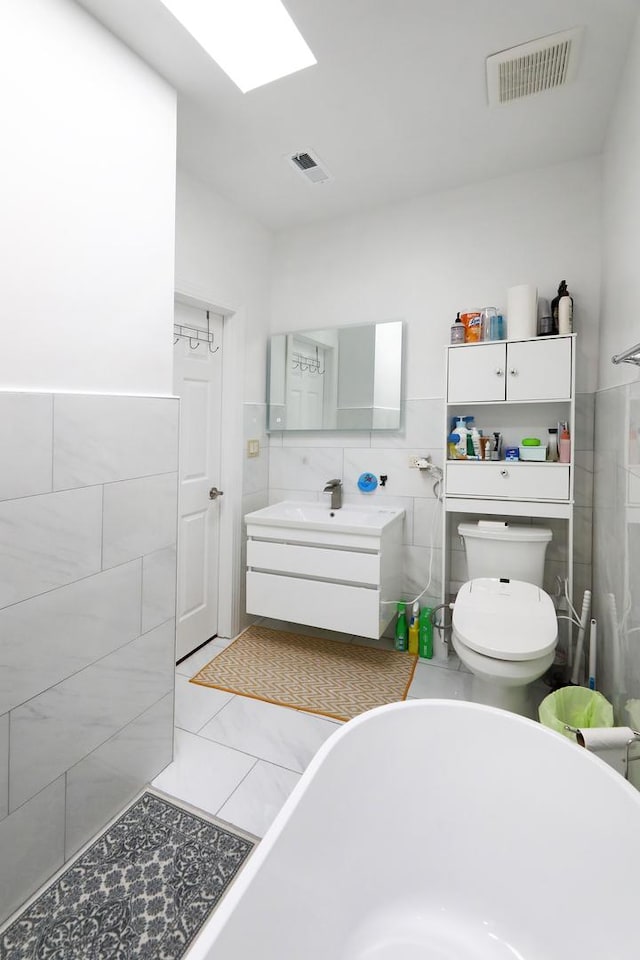 full bathroom featuring tile walls, visible vents, and a freestanding tub