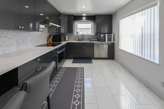kitchen featuring light countertops, dark cabinetry, backsplash, a sink, and appliances with stainless steel finishes