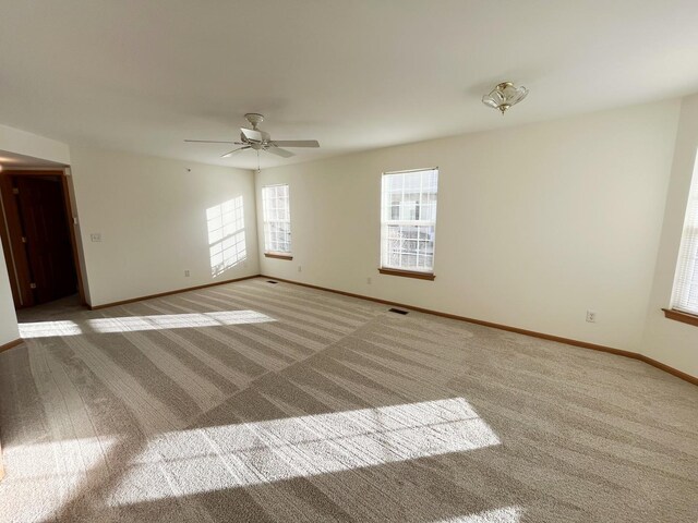 carpeted empty room featuring baseboards, visible vents, and a ceiling fan