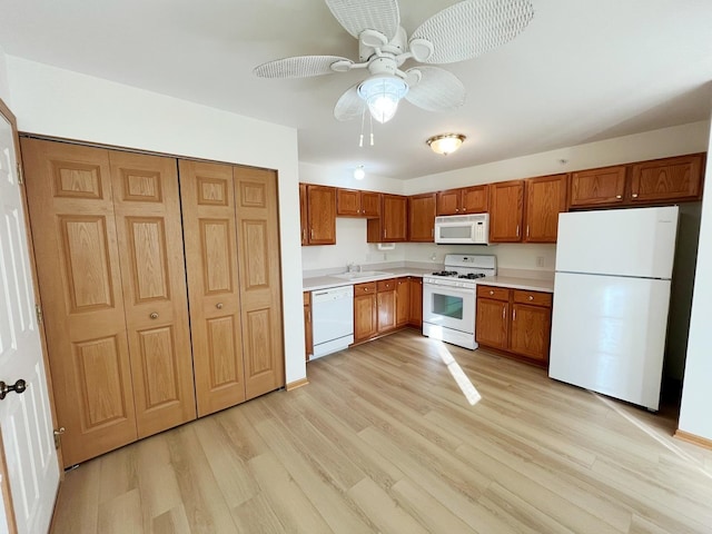 kitchen with light countertops, light wood-style flooring, white appliances, brown cabinets, and a sink