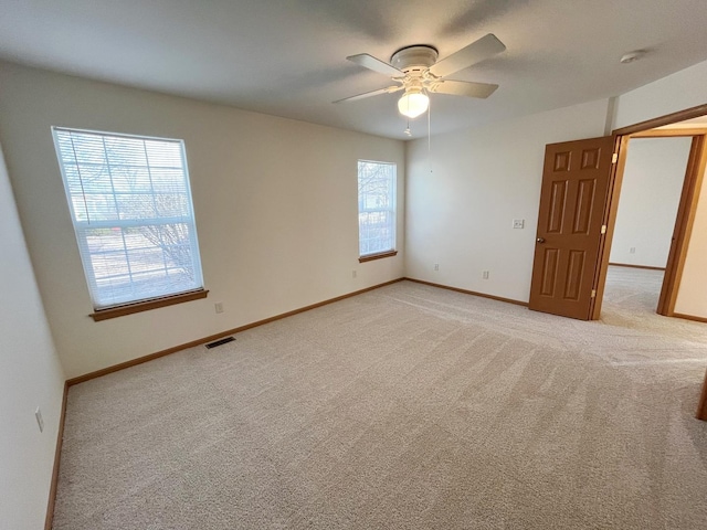 empty room featuring light colored carpet, visible vents, ceiling fan, and baseboards