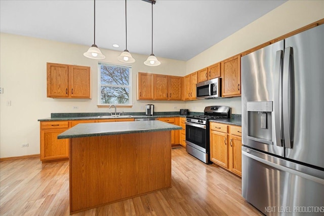 kitchen featuring a center island, dark countertops, light wood-style floors, appliances with stainless steel finishes, and a sink