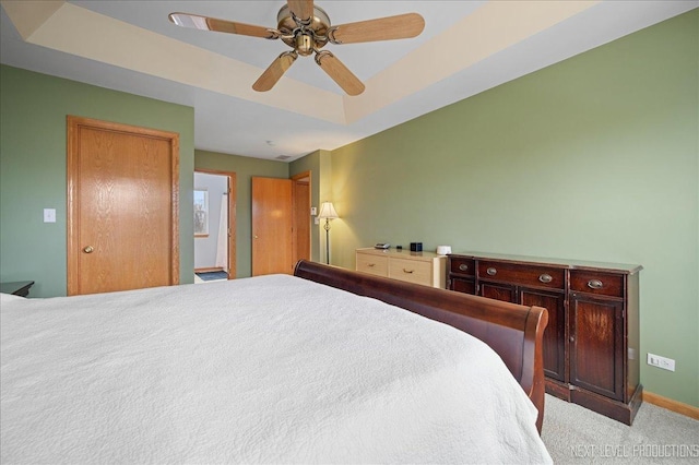 carpeted bedroom with a tray ceiling, baseboards, and a ceiling fan