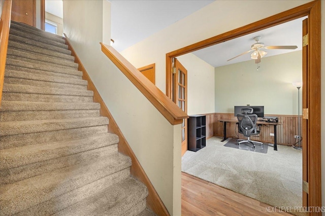 stairway featuring wooden walls, wood finished floors, a wainscoted wall, and ceiling fan