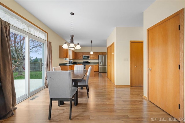 dining area featuring visible vents, baseboards, light wood-type flooring, and an inviting chandelier