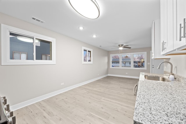 kitchen with light wood-style flooring, baseboards, a sink, visible vents, and white cabinets