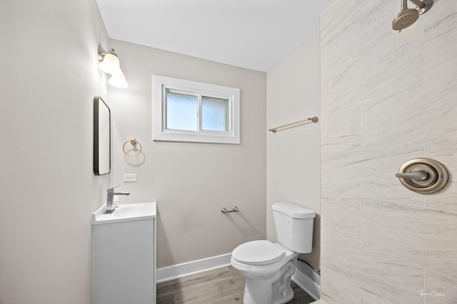 bathroom with a tile shower, toilet, vanity, wood finished floors, and baseboards