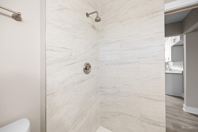 full bathroom with toilet, a tile shower, and wood finished floors