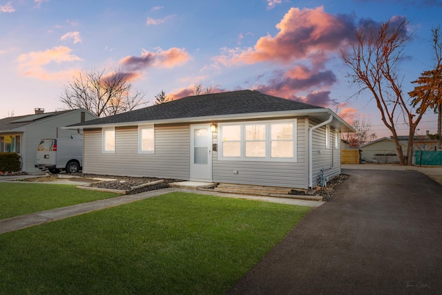 view of front of home with driveway, roof with shingles, and a front yard