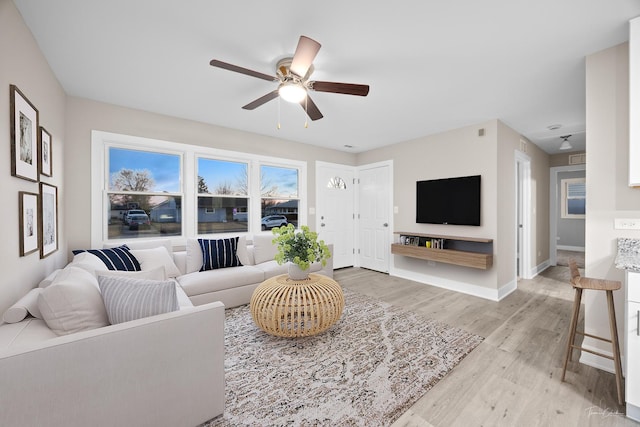 living area with baseboards, ceiling fan, and light wood-style flooring