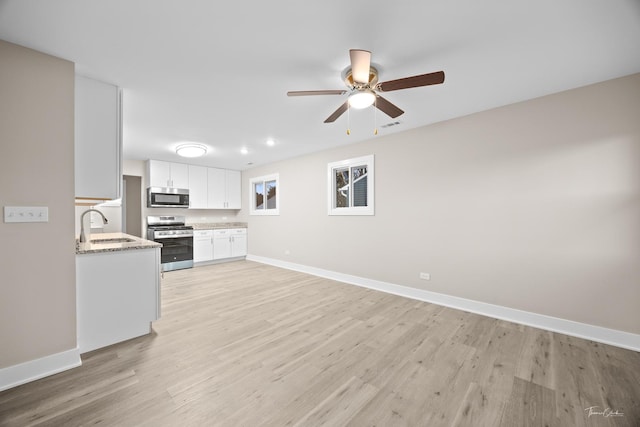 kitchen with stainless steel appliances, baseboards, a sink, white cabinets, and a ceiling fan