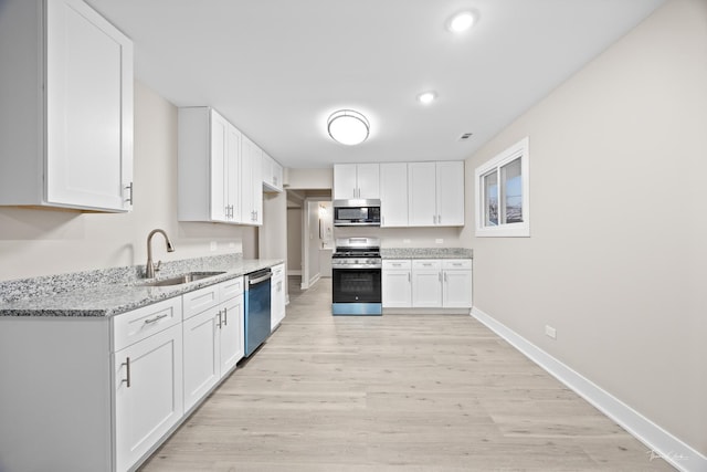 kitchen with light wood-style flooring, appliances with stainless steel finishes, white cabinetry, a sink, and light stone counters