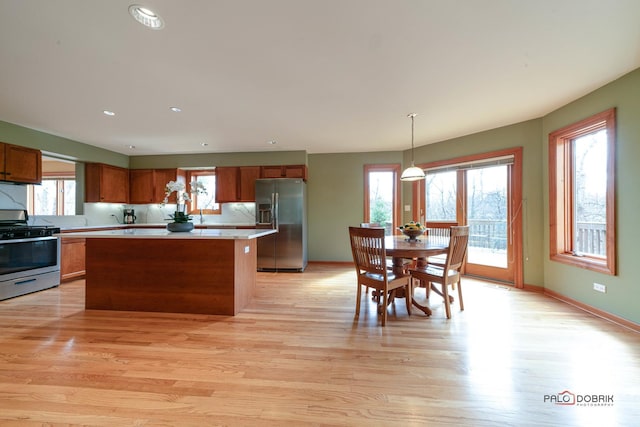 kitchen with a kitchen island, light countertops, stainless steel appliances, brown cabinets, and light wood finished floors