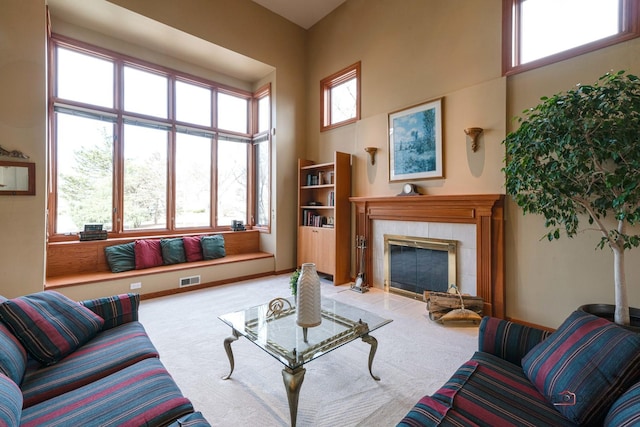 carpeted living room with a tiled fireplace, visible vents, baseboards, and a high ceiling