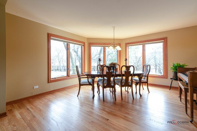 dining room with light wood-type flooring, a notable chandelier, and baseboards