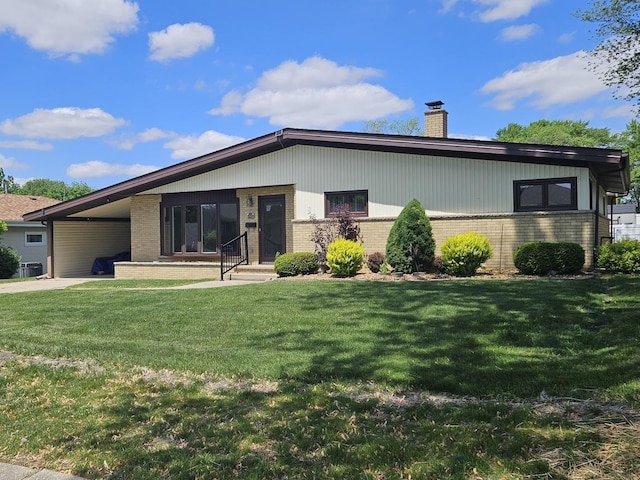 view of front facade featuring brick siding, a chimney, a front yard, and a carport