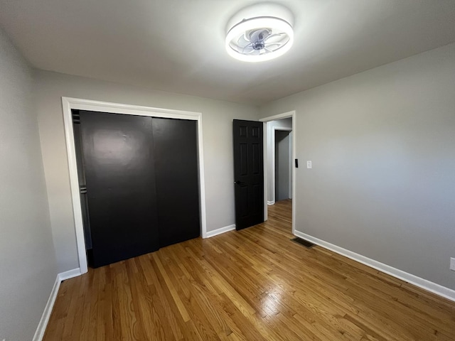 unfurnished bedroom with wood finished floors, baseboards, and a closet