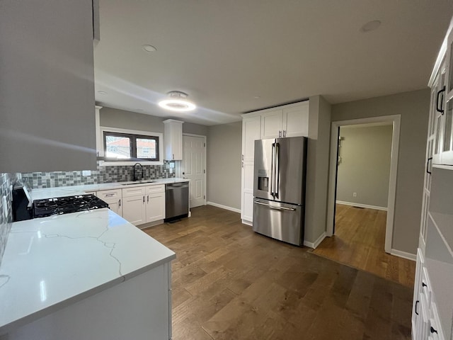 kitchen with appliances with stainless steel finishes, a sink, tasteful backsplash, light stone counters, and white cabinets