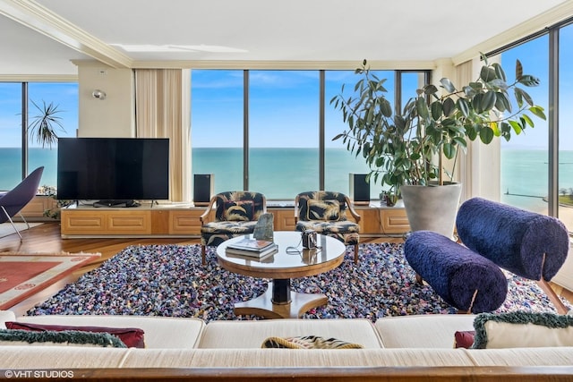living room with a water view, wood finished floors, ornamental molding, and floor to ceiling windows