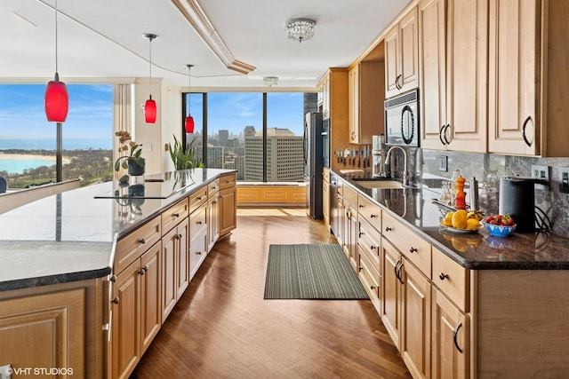 kitchen with a sink, black appliances, wood finished floors, a large island with sink, and tasteful backsplash