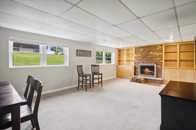 carpeted living room with a brick fireplace, baseboards, built in shelves, and a paneled ceiling