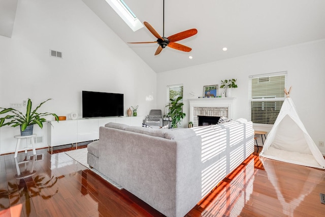 living area with high vaulted ceiling, ceiling fan, visible vents, wood finished floors, and a brick fireplace
