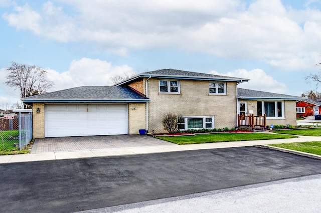tri-level home with driveway, a front lawn, brick siding, a garage, and fence