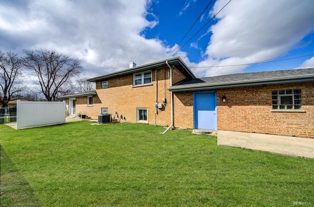 back of house with brick siding, central air condition unit, fence, and a lawn