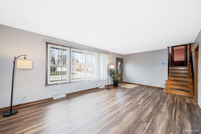unfurnished living room with stairway, visible vents, baseboards, and wood finished floors