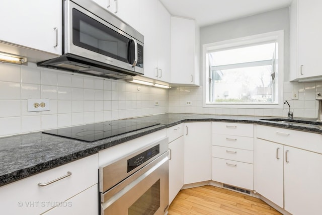 349 Ridge Rd, Kenilworth, IL 60043 - kitchen featuring light wood finished floors, dark stone counters, stainless steel appliances, white cabinets, and tasteful backsplash