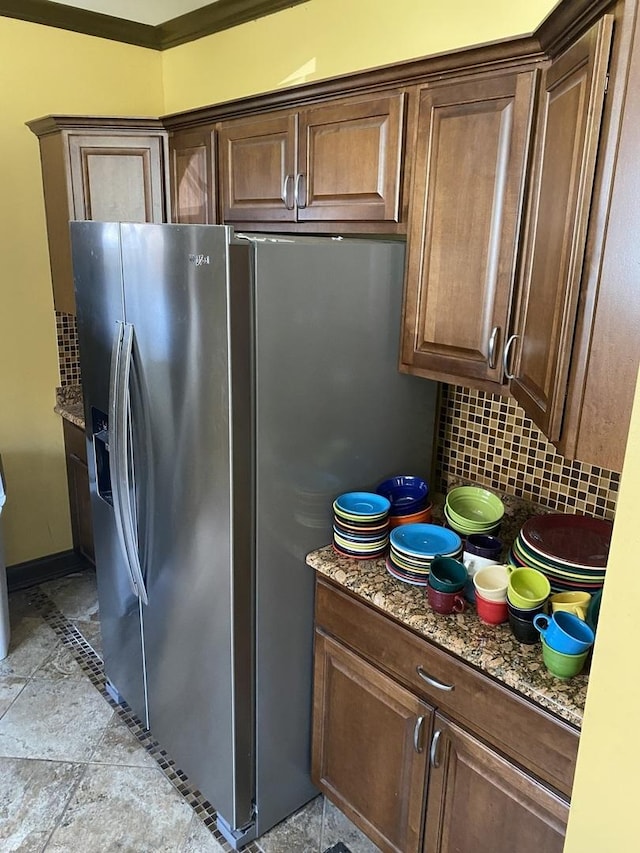 kitchen featuring tasteful backsplash, stainless steel fridge with ice dispenser, stone finish flooring, and stone counters