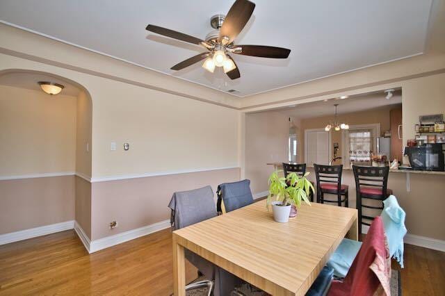 6237 N Mozart St, Chicago, IL 60659 - dining area featuring arched walkways, ceiling fan with notable chandelier, baseboards, and wood finished floors