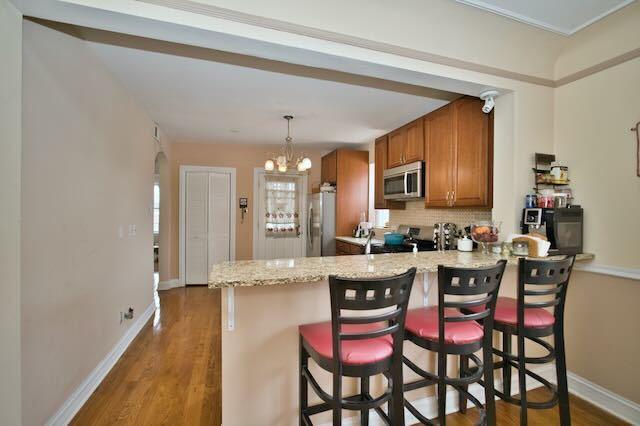 6237 N Mozart St, Chicago, IL 60659 - kitchen featuring brown cabinetry, wood finished floors, a peninsula, and stainless steel appliances