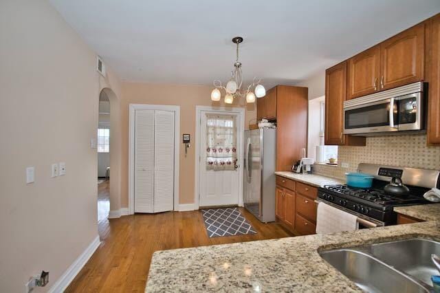 6237 N Mozart St, Chicago, IL 60659 - kitchen featuring brown cabinetry, tasteful backsplash, arched walkways, visible vents, and stainless steel appliances