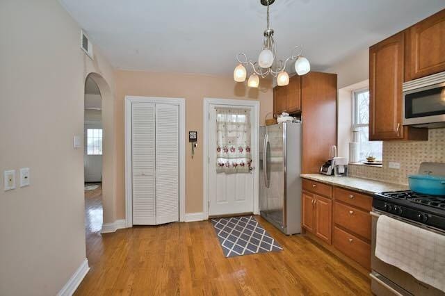 6237 N Mozart St, Chicago, IL 60659 - kitchen with visible vents, arched walkways, light wood-type flooring, appliances with stainless steel finishes, and brown cabinets