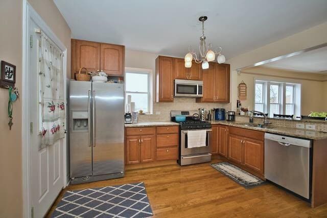 6237 N Mozart St, Chicago, IL 60659 - kitchen featuring brown cabinetry, light wood finished floors, a sink, and stainless steel appliances
