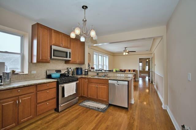 6237 N Mozart St, Chicago, IL 60659 - kitchen with a peninsula, wood finished floors, a sink, stainless steel appliances, and brown cabinets