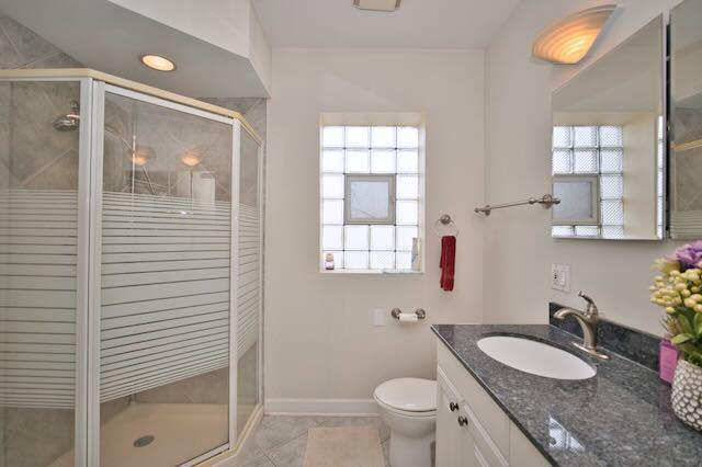6237 N Mozart St, Chicago, IL 60659 - bathroom with vanity, tile patterned flooring, toilet, a stall shower, and baseboards