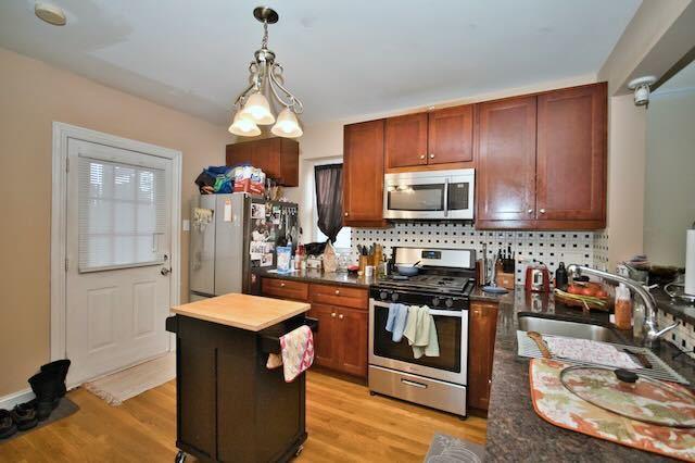 6237 N Mozart St, Chicago, IL 60659 - kitchen with light wood-type flooring, dark countertops, decorative light fixtures, appliances with stainless steel finishes, and a sink
