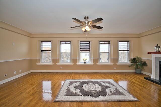 6237 N Mozart St, Chicago, IL 60659 - unfurnished living room with a healthy amount of sunlight, ceiling fan, a fireplace with raised hearth, and wood finished floors